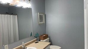 Een badkamer met een spiegel, wastafel, toilet en een mandje op de achterkant van het toilet.