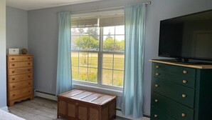 A room with a large window, a television on a stand, a wooden dresser, and a bench. - Abenaki Retreat on Matinicus Island (Matinicus)