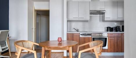 Uma cozinha compacta com eletrodomésticos modernos, duas cadeiras de madeira e uma mesa pequena.