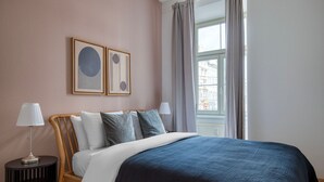 A neatly arranged bedroom with a bed, two bedside lamps, a small side table, and a window with curtains.