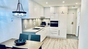 A modern kitchen with white cabinets, a built-in oven, and a dining area with a table and chairs. - Main Village • 1 Bedroom • Queen+2 Sofabeds • AC • Laundry • Parking • EV • Reno (Whistler)
