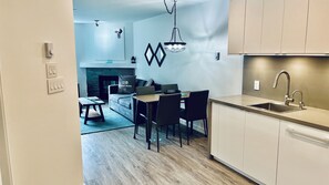 A modern kitchen with a built-in oven, a dining area with a table and chairs, and a living room with a sofa and a fireplace. - Main Village • 1 Bedroom • Queen+2 Sofabeds • AC • Laundry • Parking • EV • Reno (Whistler)
