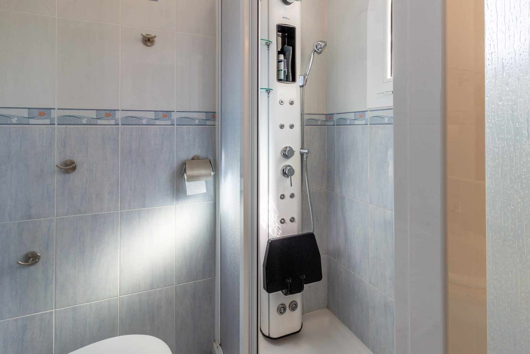 A shower enclosure with a handheld showerhead, a towel rack, and a toilet paper holder.