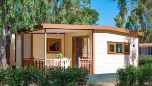 A small, single-story building with a porch, a small table, and chairs, surrounded by greenery. - Nice apartment in villa for 4 people with WIFI, pool, A/C, TV and terrace (Alghero)