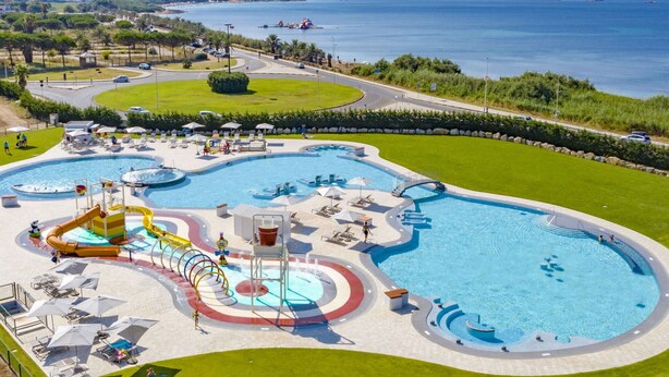 A large outdoor swimming pool with multiple water features and a surrounding grassy area. - Nice apartment in villa for 4 people with WIFI, pool, A/C, TV and terrace (Alghero)