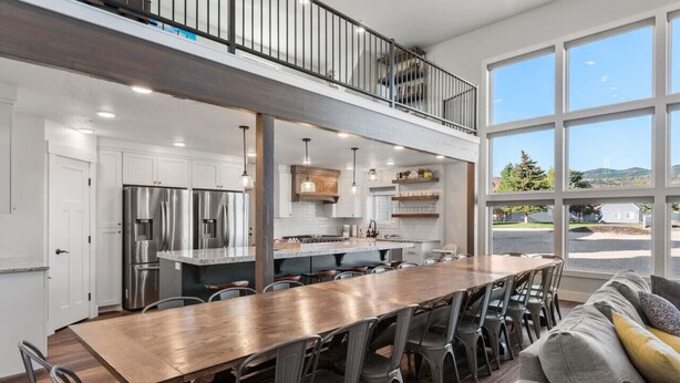 Una cocina amplia con una larga mesa de madera y sillas, un balcón con barandilla y ventanas grandes que ofrecen vistas al exterior.