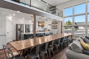 Una cocina amplia con una larga mesa de madera y sillas, un balcón con barandilla y ventanas grandes que ofrecen vistas al exterior.