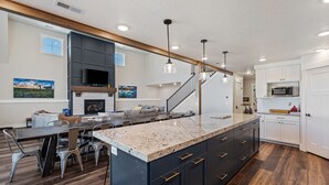 Una cocina moderna con una isla grande, armarios oscuros y un comedor con una mesa larga y sillas.