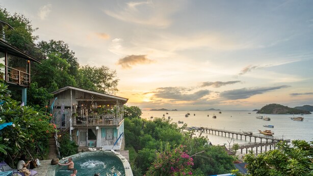 A pool area with a view of the sea and boats, surrounded by lush greenery and a wooden building. - Selini Hills (Labuan Bajo)