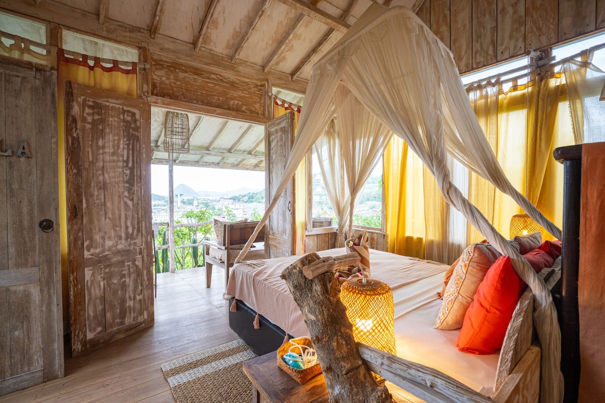 A room with a bed under a canopy, wooden walls, and a view of the outdoors.
