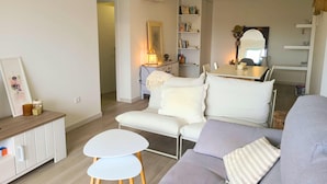 En moderne stue med en sofa, et lille hvidt bord og et spiseområde med bord og stole.