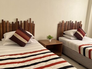 A hotel room with two beds, each with striped bedding and wooden headboards. There is a small table with a plant between the beds.
