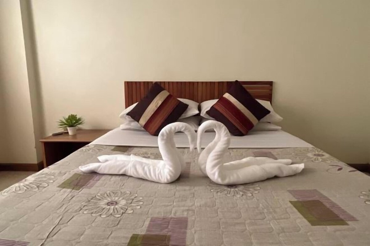 A neatly made bed with a floral bedspread and two swan-shaped pillows.