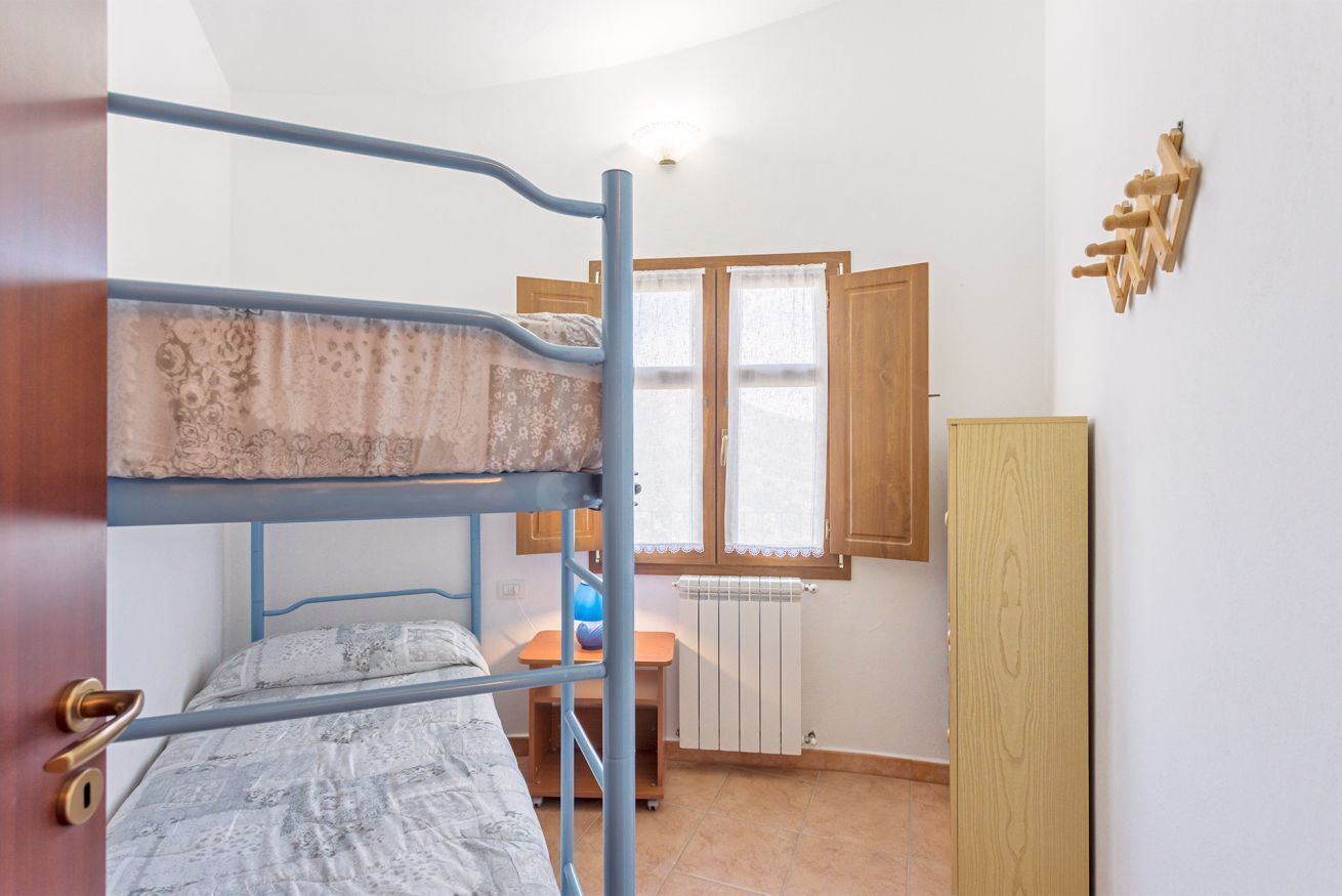Une chambre avec un lit superposé, une fenêtre, un radiateur et une armoire en bois.