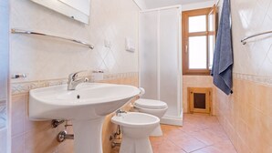 Een badkamer met een wastafel, toilet en bidet, betegelde wanden en een raam.