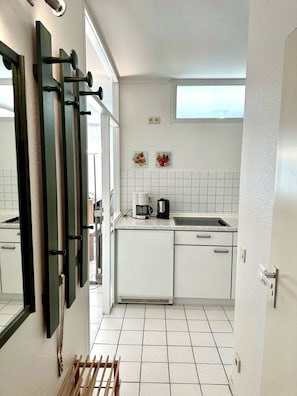 Cocina compacta con armarios blancos, cafetera y ventana sobre el fregadero.