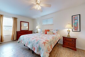 A bedroom with a bed, two nightstands, a ceiling fan, a window with curtains, a mirror, and a framed picture on the wall.