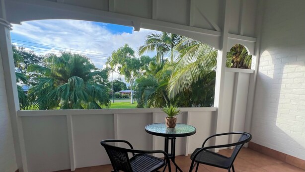 A balcony with two chairs and a small table, overlooking a garden with palm trees and a clear sky. - Sans Souci Apartments (Ingham)