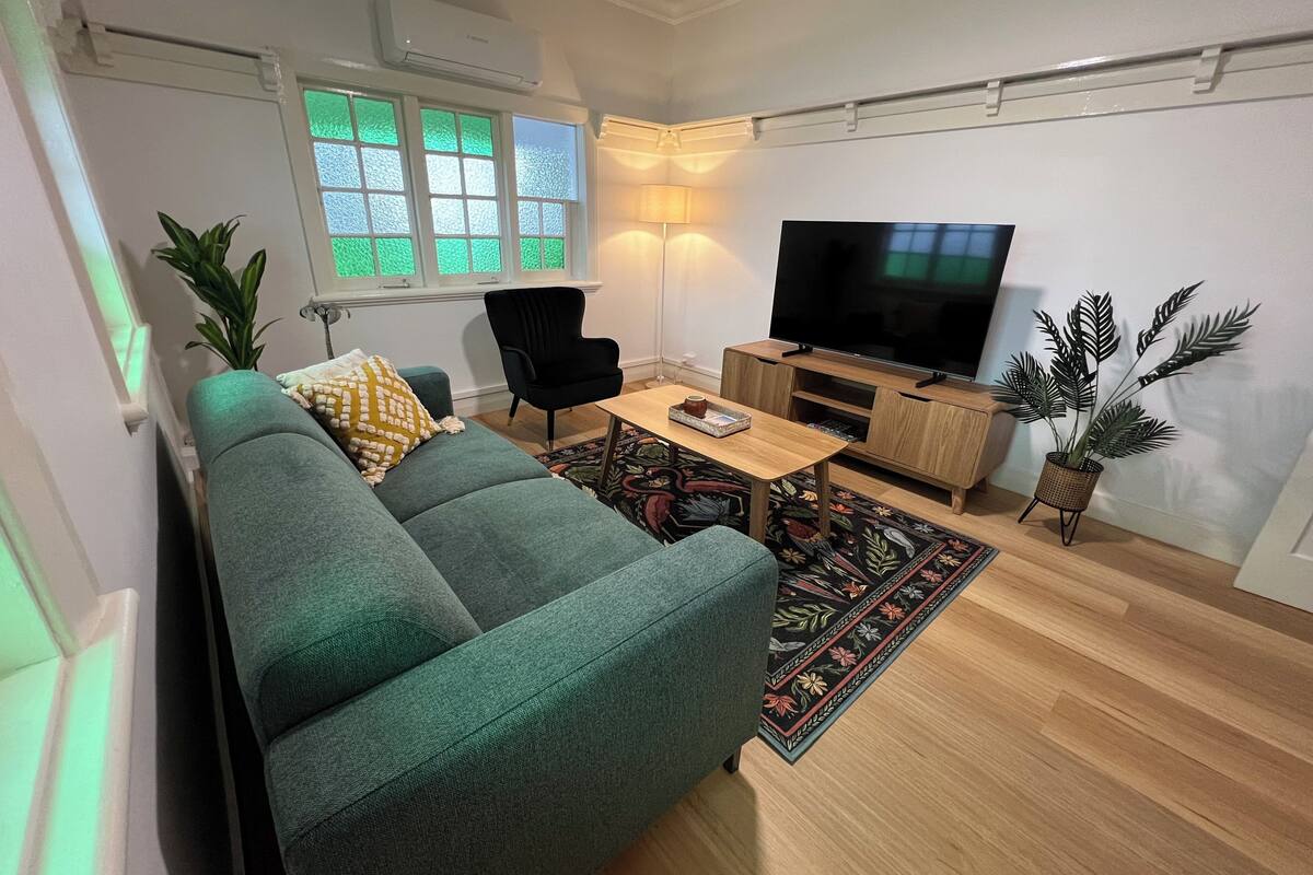 Ein modernes Wohnzimmer mit einem grünen Sofa, einem schwarzen Sessel, einem Holztisch, einem Flachbildfernseher und einer Zimmerpflanze.
