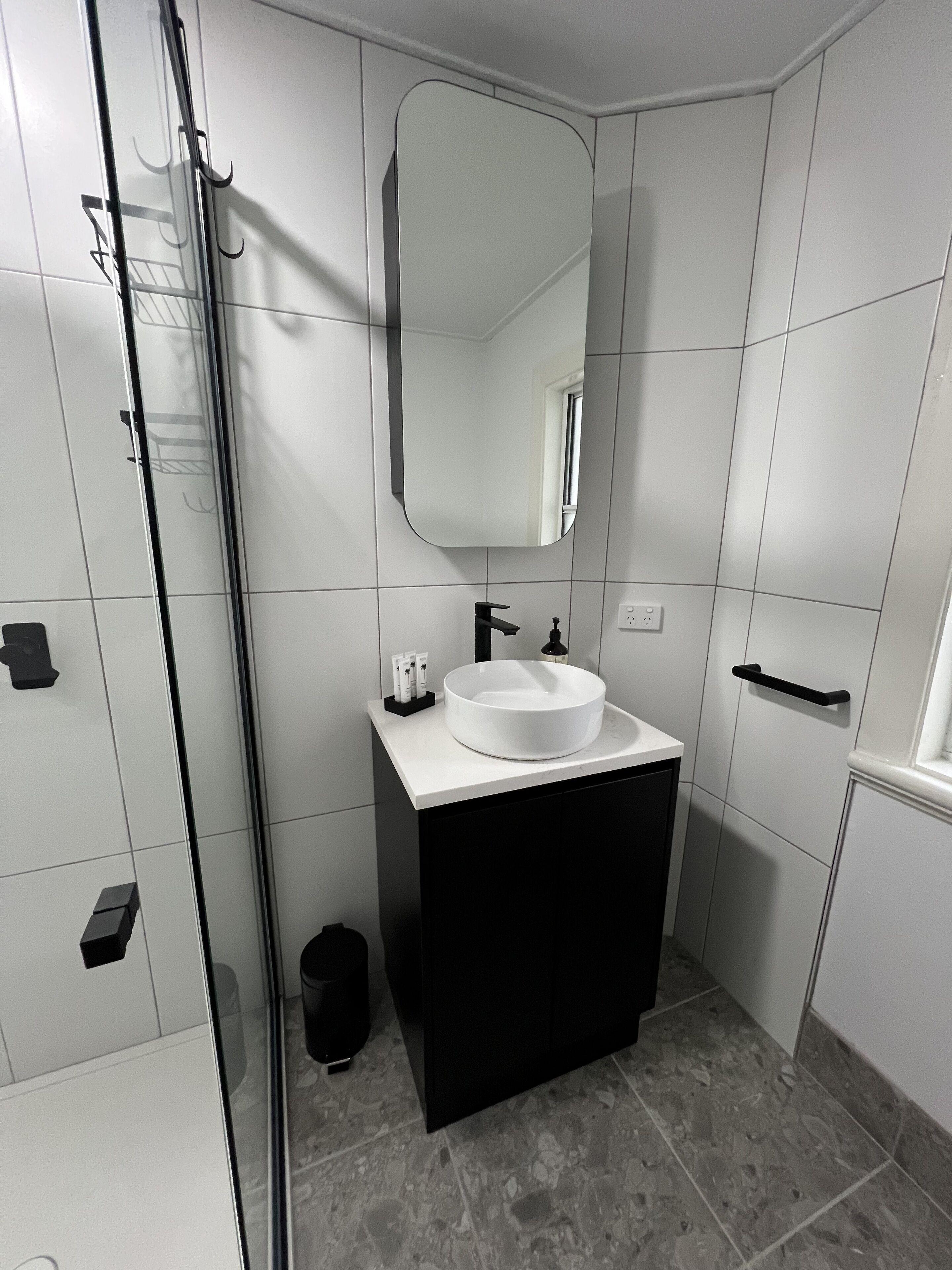 A modern bathroom with a glass shower enclosure, a white sink, and a black vanity.