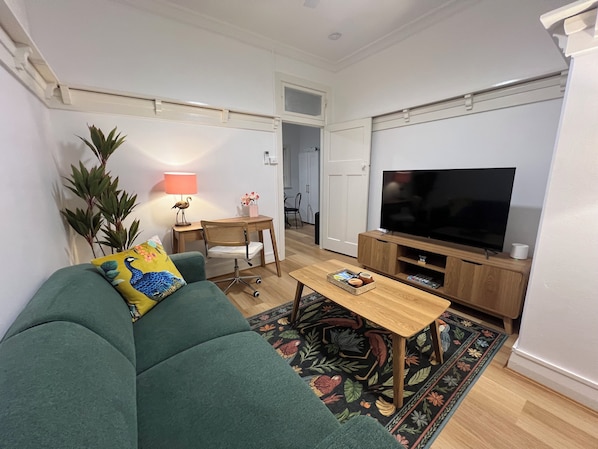 A living room with a green sofa, a wooden coffee table, a TV, and a desk with a lamp. - Sans Souci Apartments (Ingham)