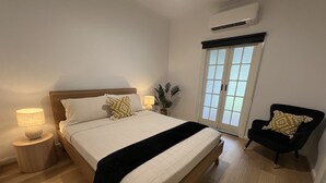 A bedroom with a bed, bedside lamps, a chair, a potted plant, and a window with a view. - Sans Souci Apartments (Ingham)