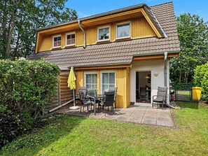 A two-story house with a patio area, a dining table with chairs, and a yellow umbrella.