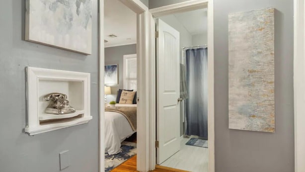 A hallway with a bed, a door leading to a bathroom, and a shelf with a decorative item.