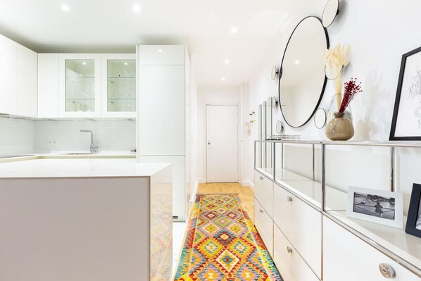 A modern kitchen with white cabinets, a central island, and a colorful patterned rug.