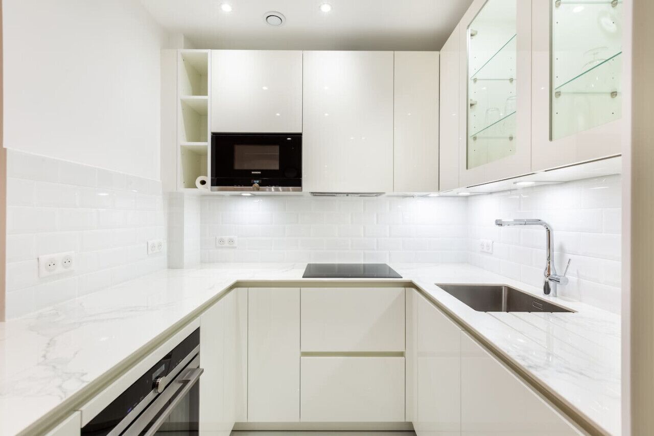 Una cocina moderna con armarios blancos, un microondas negro y un lavabo de acero inoxidable.