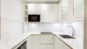 A modern kitchen with white cabinetry, a black microwave, and a stainless steel sink. - Passy - 1 chambre - 2 lits (Paris)