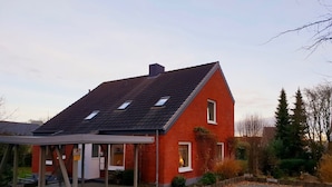 Une maison en briques rouges, avec un toit en pente, un porche abrité et une allée gravillonnée.