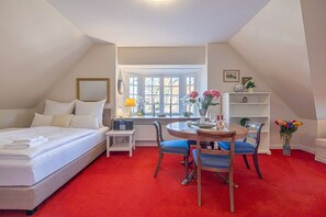 Quarto com cama, escrivaninha, cadeira, janela e tapete vermelho.