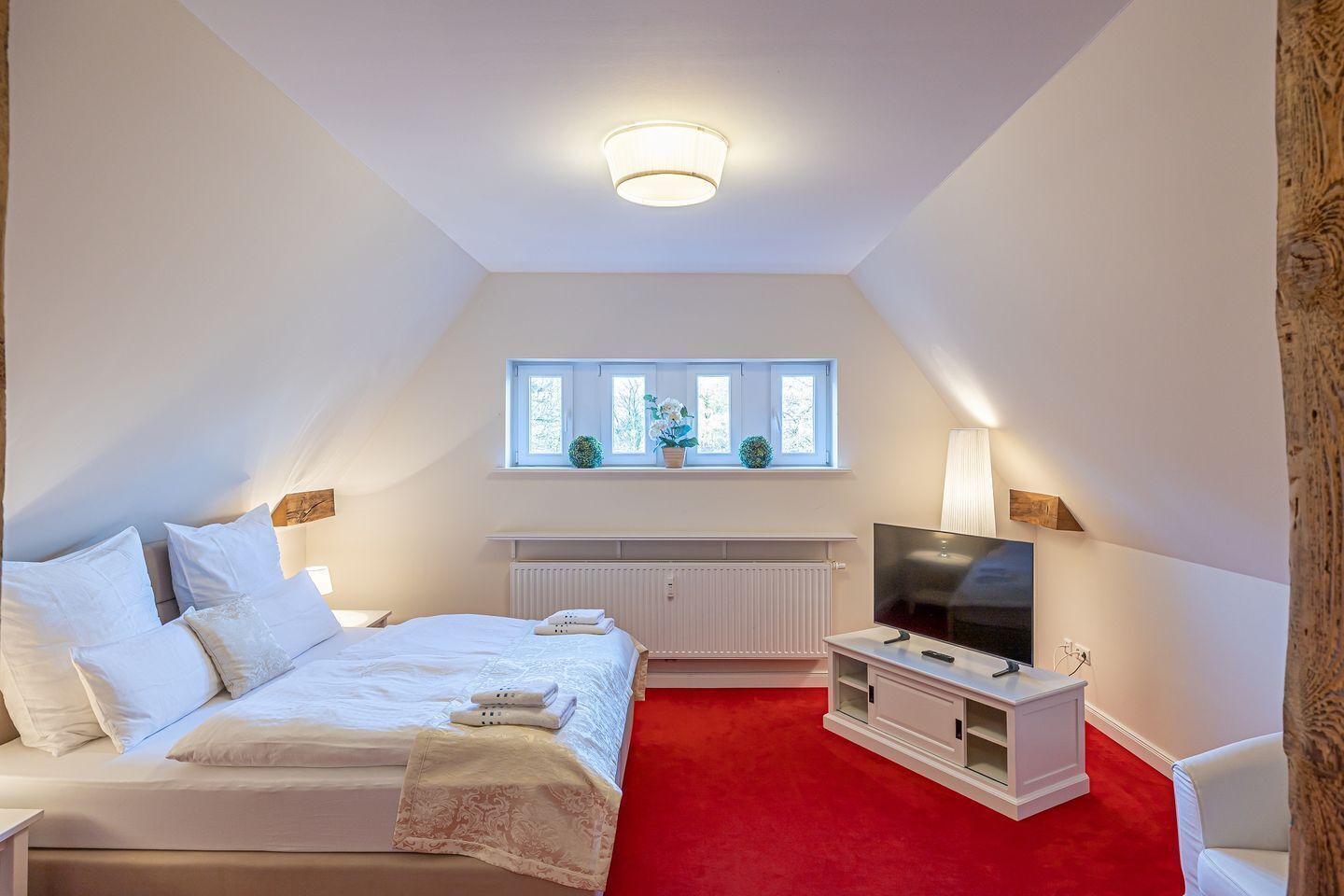 Ein Schlafzimmer mit Bett, Fernseher, Fenster und einem roten Teppich.