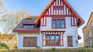 Una casa de dos pisos con techo a dos aguas pronunciado, marcos de ventana rojos y paredes blancas.