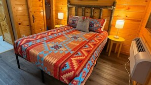 A wooden cabin room with a bed, two bedside tables, a lamp, and an air conditioner. - 9 on the Ridge - 3 miles from Dollywood & Pet Friendly - Many repeat customers! (Pigeon Forge)
