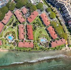 An aerial view of a resort with multiple red-roofed buildings, a beach, and a pool area. - Remodeled Direct Oceanfront Studio Getaway-Papakea A306 (Lahaina)