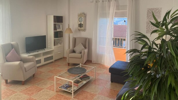 A living room with a television, bookshelf, armchair, coffee table, and a view of the outside.