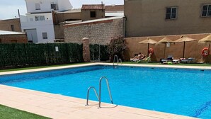 A swimming pool with a metal ladder, surrounded by a green lawn and a stone wall.