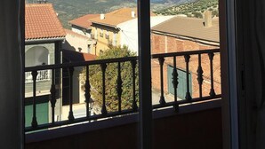 A balcony with a view of a mountainous landscape and terracotta-roofed buildings.