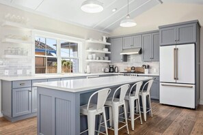 A modern kitchen with a large island, bar stools, grey cabinets, and a white refrigerator. - "Endless Summer" Home - stunning ocean views! (Santa Cruz)