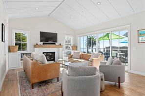 A spacious living room with a fireplace, comfortable seating, and large windows offering a view of palm trees.