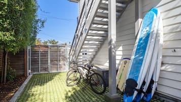 Un espace extérieur abrité où l’on aperçoit un vélo et des planches de surf appuyées contre un bâtiment.