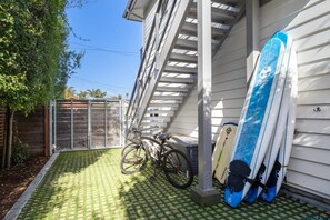 A covered patio with a bicycle and surfboards leaning against a house.