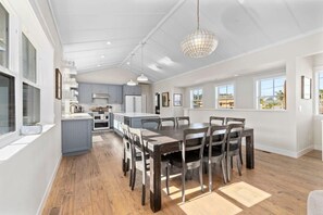 A spacious kitchen with a dining area, large windows, and a chandelier.