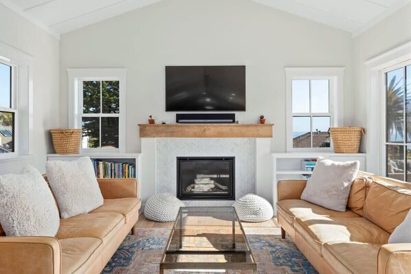 A living room with a fireplace, a large TV mounted above it, and two sofas with cushions.