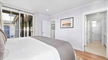 Un dormitorio con cama, una puerta que da a un pasillo y una ventana.