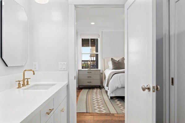 A narrow hallway with a white vanity, a gold faucet, and a window with blinds.