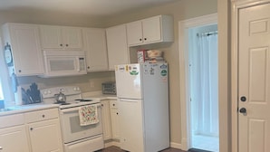 A kitchen with white cabinets, a microwave, stove, and refrigerator. There is a rug on the floor and a door leading to another room. - Entire rental unit in Warren, Rhode Island Unit 3 (Warren)