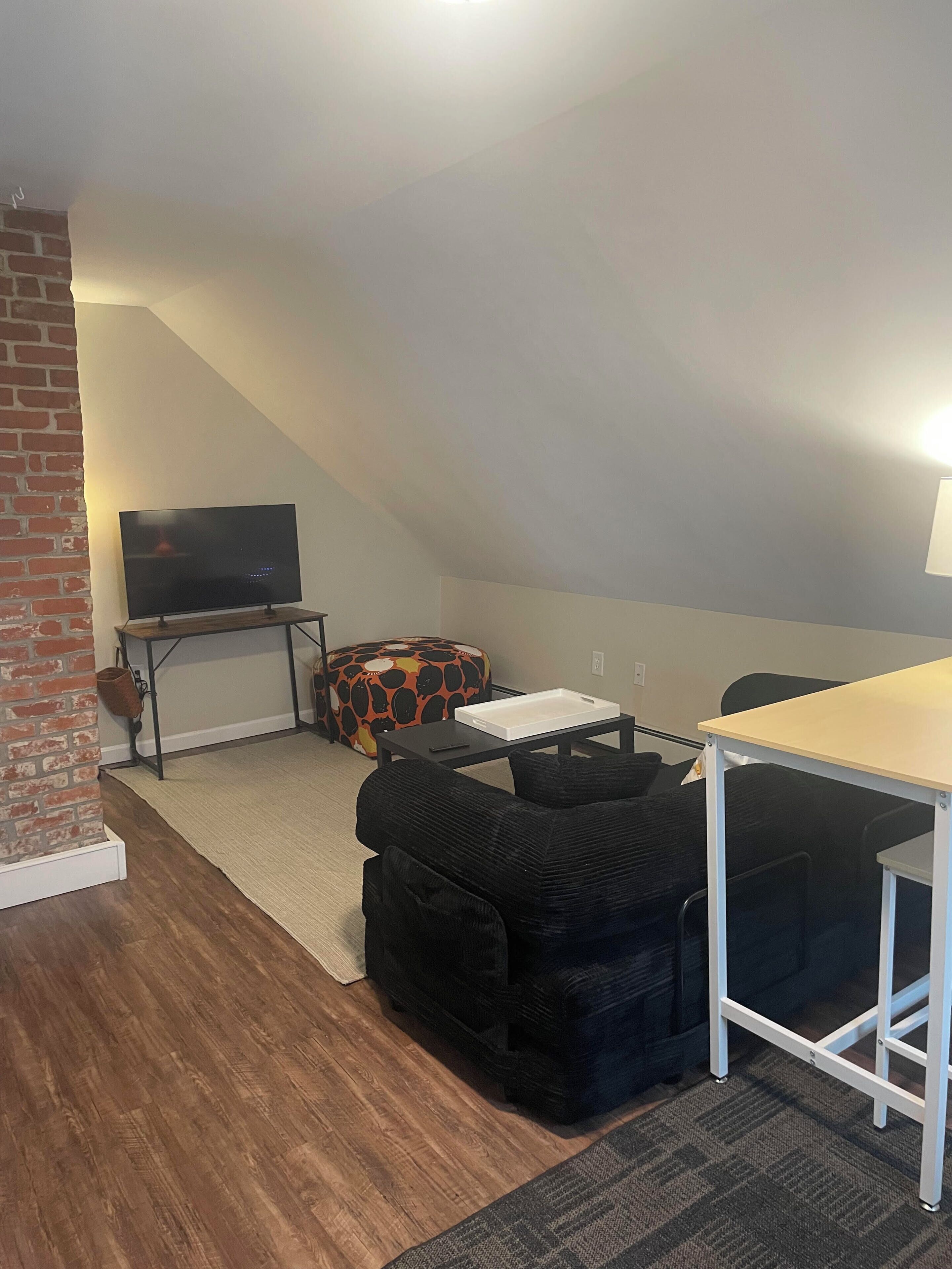 Une pièce de style loft, dotée d’une télévision, d’une petite table, d’un canapé et d’un tapis.